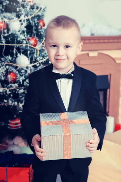 Jongen in de buurt van een kerstboom met een gift op hand. — Stockfoto