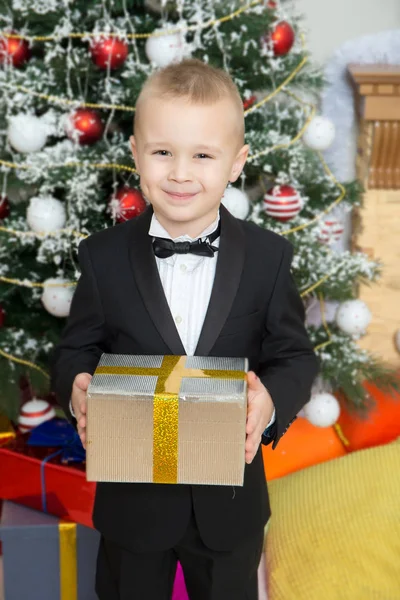 Αγόρι κοντά ένα χριστουγεννιάτικο δέντρο με ένα δώρο στο χέρι. — Φωτογραφία Αρχείου