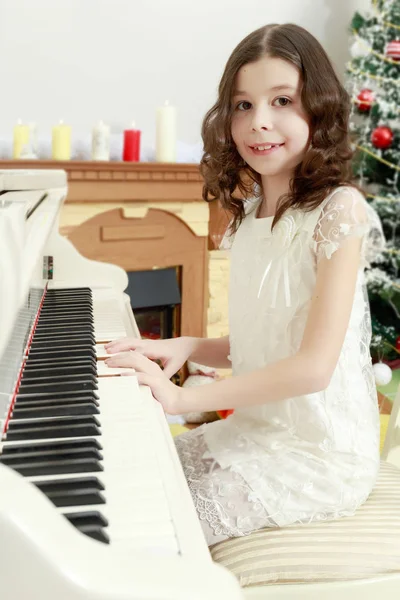 Menina bonita em um vestido branco sentado ao piano . — Fotografia de Stock