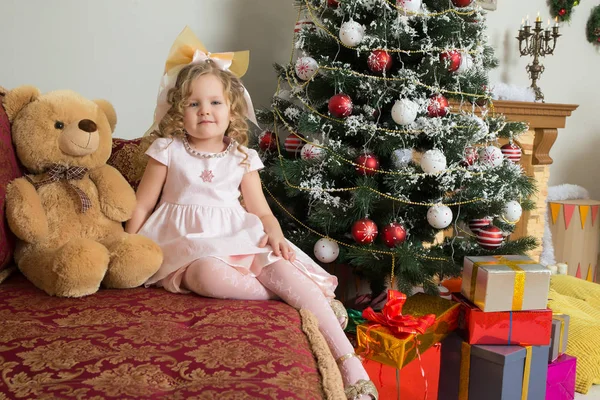 テディベアとクリスマス ツリーの近くソファに座っている女の子. — ストック写真