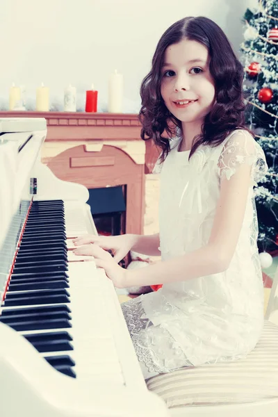 Vacker flicka i en vit klänning som sitter vid pianot. — Stockfoto
