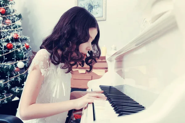Schönes Mädchen in einem weißen Kleid am Klavier sitzend. — Stockfoto