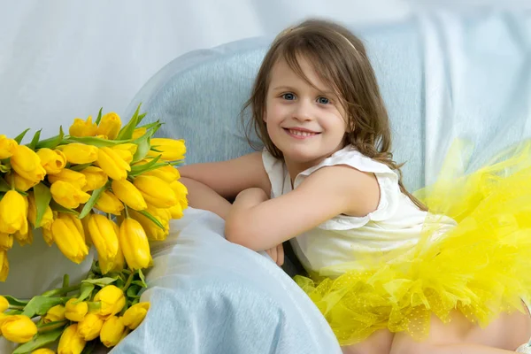 Feliz niña sentada en el sofá cerca del gran ramo de tu — Foto de Stock