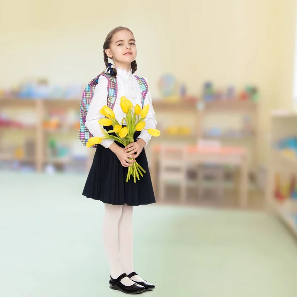 En skolflicka med en bukett blommor och en ryggsäck på hennes sho — Stockfoto