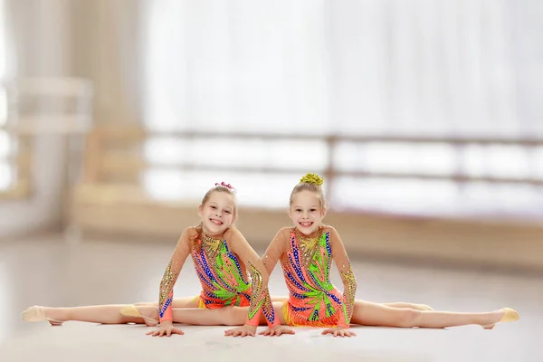 Två flickor gymnast sitter på splittringar. — Stockfoto