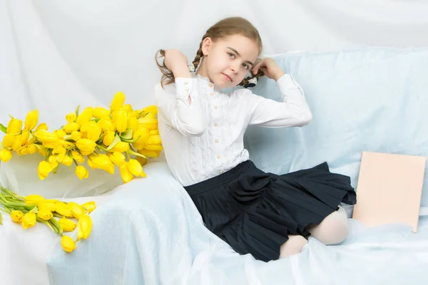 A diligent schoolgirl student with yellow tulips is sitting on t — Stock Photo, Image