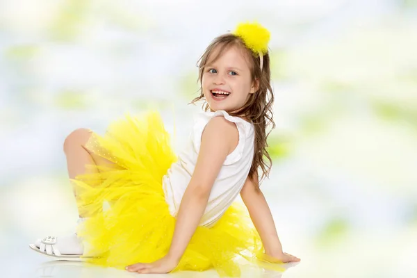 Dziewczynka w żółtą spódnicę siedzi na podłodze. — Zdjęcie stockowe