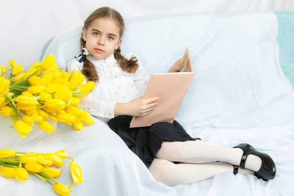 Una studentessa diligente con tulipani gialli è seduta su t — Foto Stock