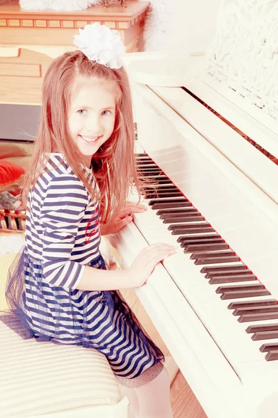 Flicka leende sitter bakom tangenterna av en stor vit piano. — Stockfoto