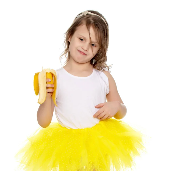 A menina na saia amarela comendo uma banana . — Fotografia de Stock