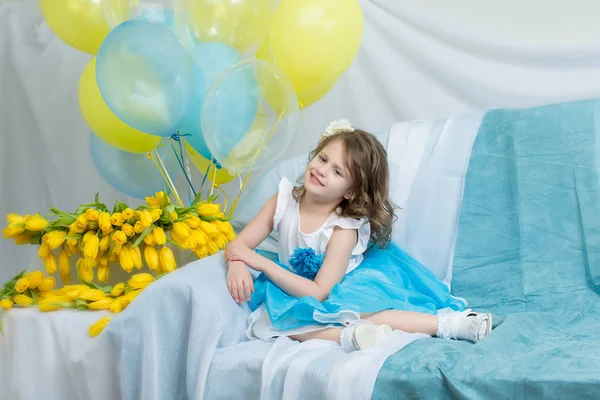 The little girl on the sofa with a bouquet of flowers. — Stock Photo, Image