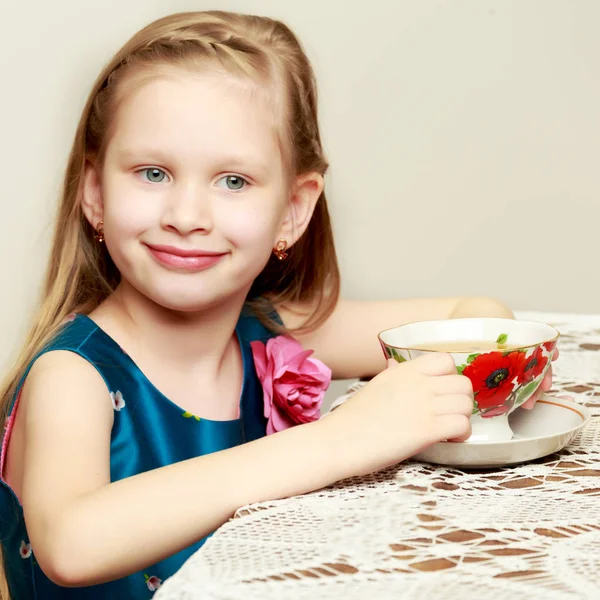 Ein schönes kleines Mädchen mit langen blonden Haaren sitzt an einem Tisch — Stockfoto