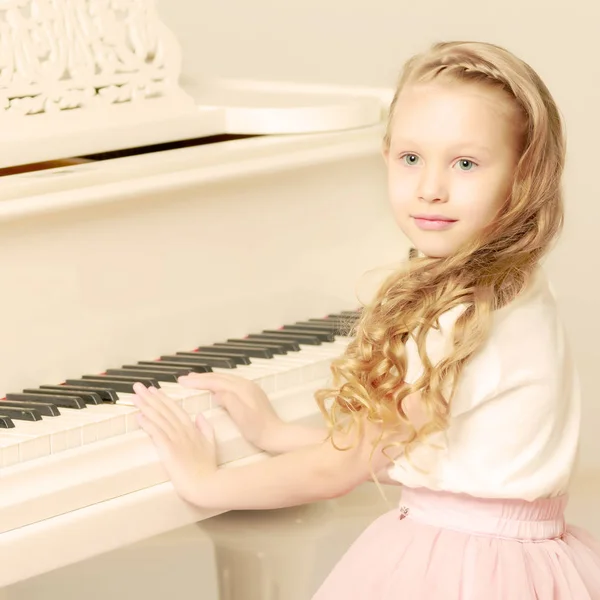 En liten flicka sitter på vita pianot. — Stockfoto