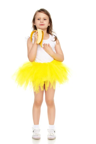 在吃一根香蕉的黄色裙子的小女孩. — 图库照片