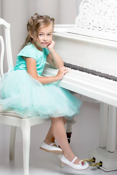 Belle petite fille joue sur un piano à queue blanc. — Photo
