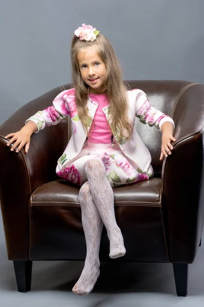 Ένα κοριτσάκι κάθεται σε μια δερμάτινη καρέκλα. — Φωτογραφία Αρχείου