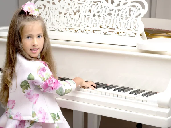 Beautiful little girl is playing on a white grand piano.