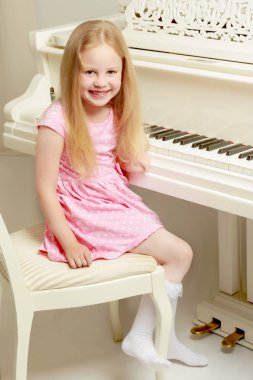 Güzel küçük kız beyaz bir piyanoda çalıyor..