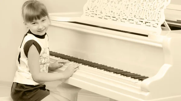 Beautiful little girl is playing on a white grand piano.