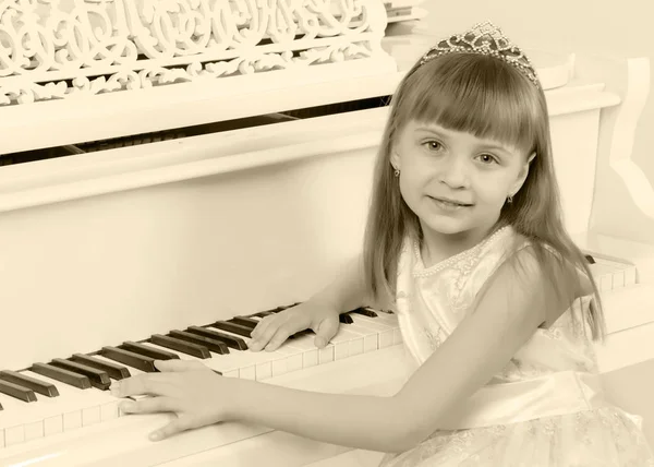 Uma menina está posando perto de um piano de cauda branco . — Fotografia de Stock