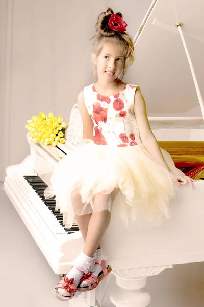 En vacker liten flicka spelar på en vit flygel. — Stockfoto