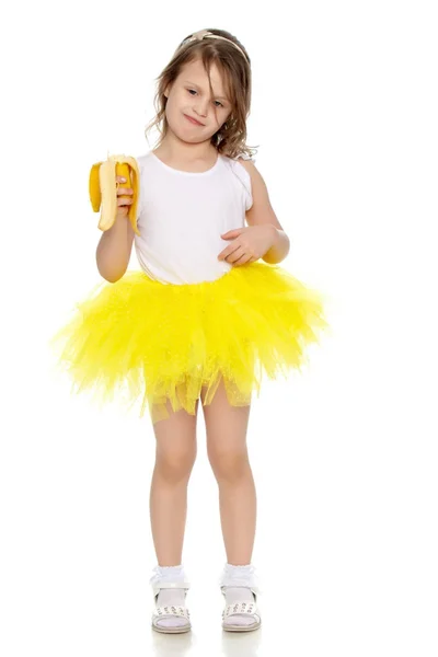 The little girl in the yellow skirt eating a banana. — Stock Photo, Image
