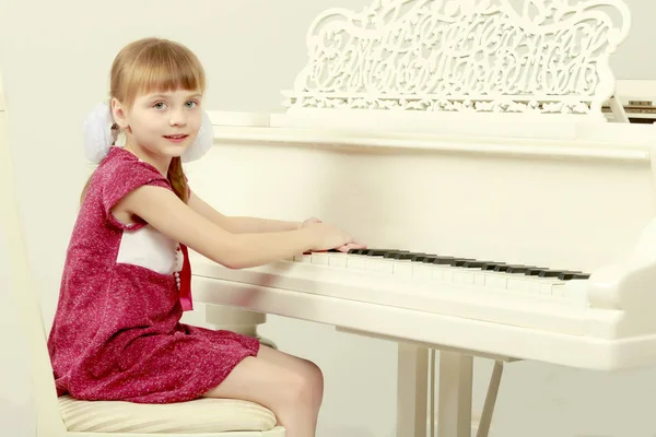 Uma menina está sentada na frente de um piano branco . — Fotografia de Stock