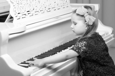 Güzel küçük kız beyaz bir piyanoda çalıyor..