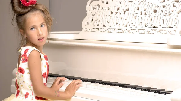 Beautiful little girl is playing on a white grand piano.