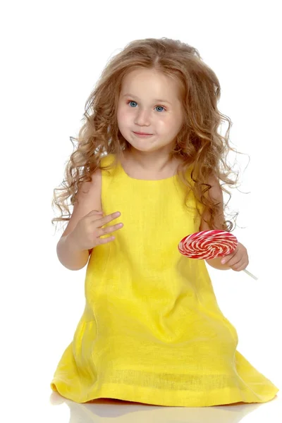 Uma menina lambe um doce em um pau . — Fotografia de Stock