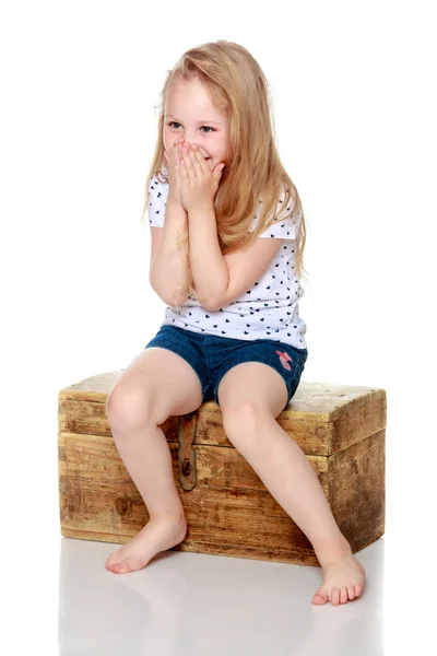 Een klein meisje zit op een houten doos.. — Stockfoto