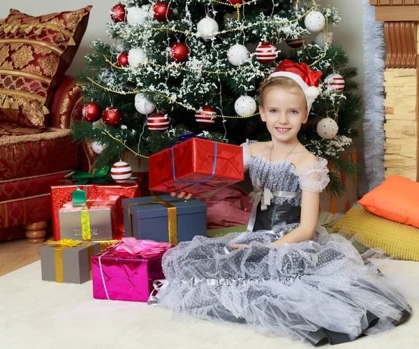 Menina sentada perto da árvore de Natal com um grande presente . — Fotografia de Stock