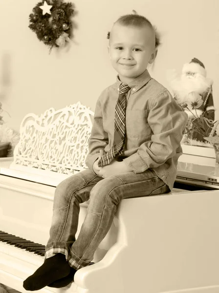 Pojken sitter på en vit piano — Stockfoto