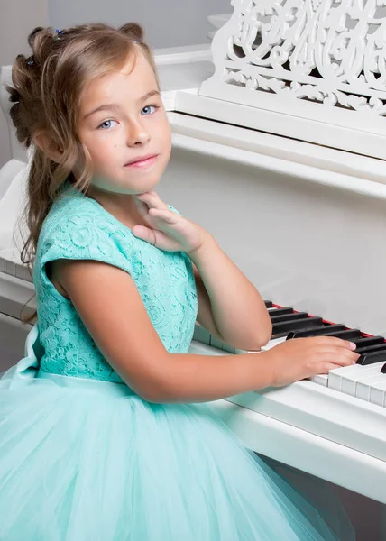 Menina bonita está tocando em um piano de cauda branco. — Fotografia de Stock