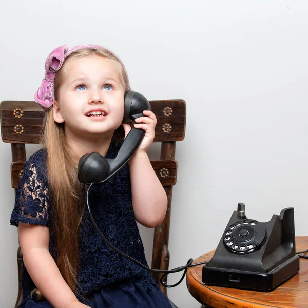 En liten flicka ringer i den gamla telefonen.. — Stockfoto