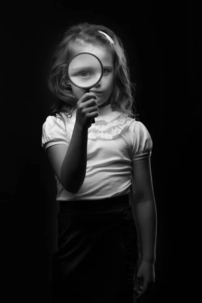 En liten flicka ser genom ett förstoringsglas — Stockfoto