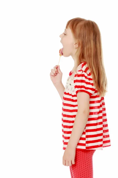 A little girl licks a candy on a stick. — Stock Photo, Image