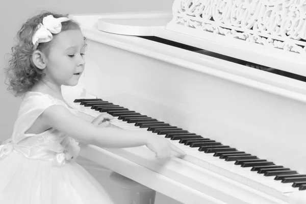 Beautiful little girl is playing on a white grand piano.