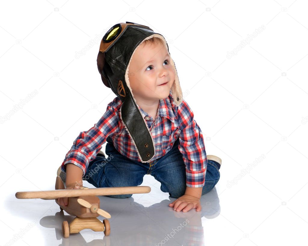 A little boy in a pilots cap and a wooden plane in his hand