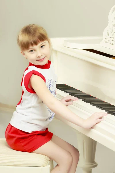Hermosa niña está tocando en un piano de cola blanco. — Foto de Stock