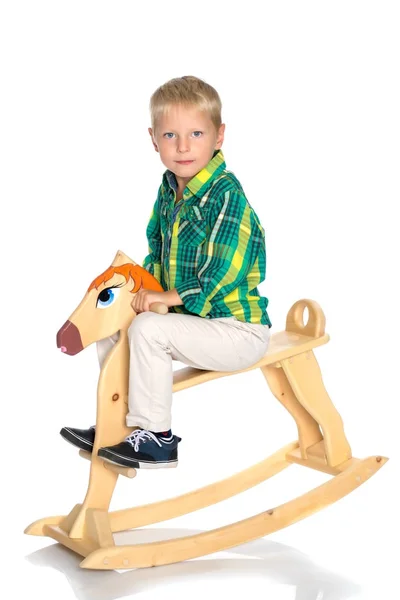 Um menino está montando um cavalo de madeira — Fotografia de Stock