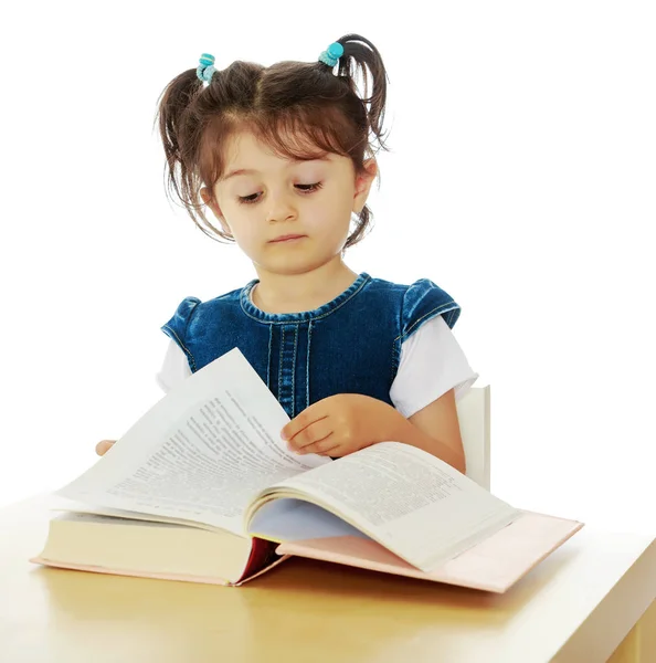 Mała dziewczynka czytająca książkę przy stole. — Zdjęcie stockowe