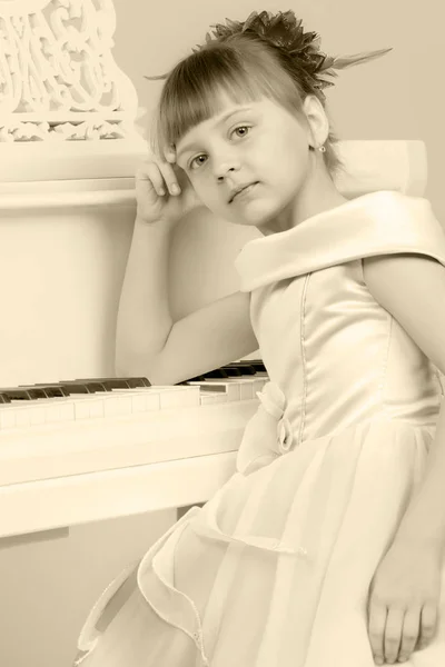 Uma menina está posando perto de um piano de cauda branco . — Fotografia de Stock