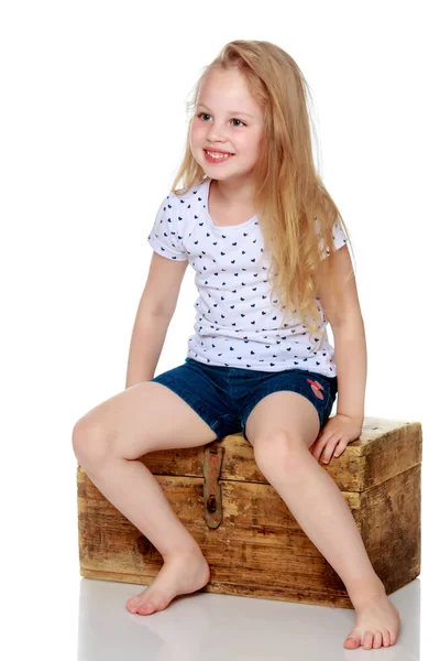 Una niña está sentada en una caja de madera . — Foto de Stock
