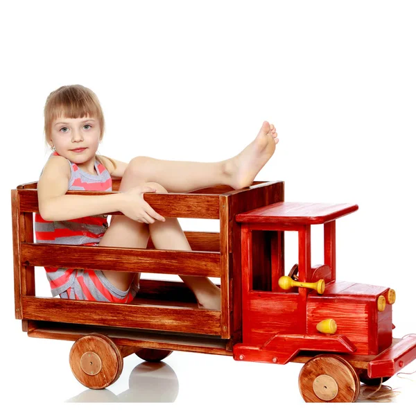 Das Mädchen sitzt auf einem großen Spielzeugauto aus Holz. — Stockfoto