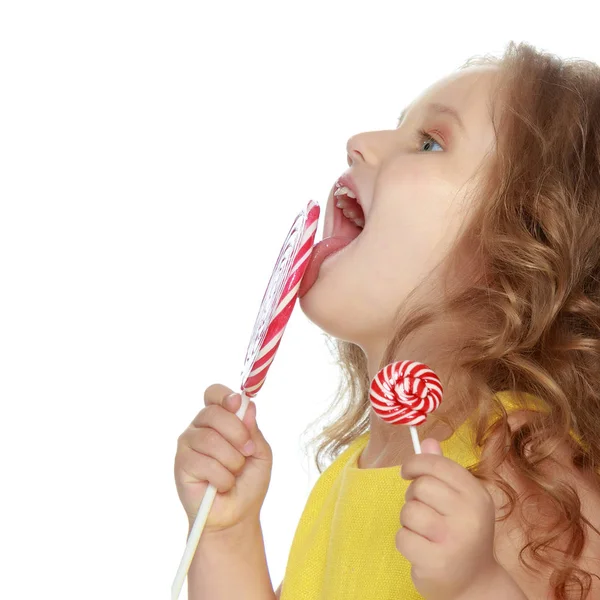 Een klein meisje likt een snoepje op een stick. — Stockfoto