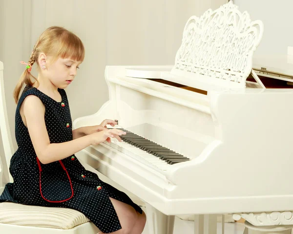 Beautiful little girl is playing on a white grand piano.