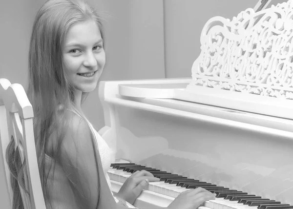 A teenage girl is playing on a white grand piano.