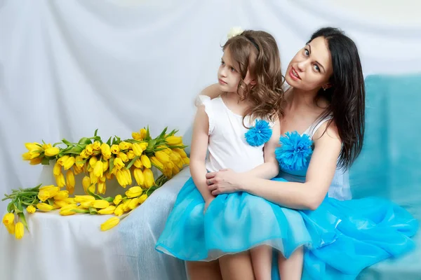 Maman et fille sur le canapé avec un bouquet de fleurs . — Photo