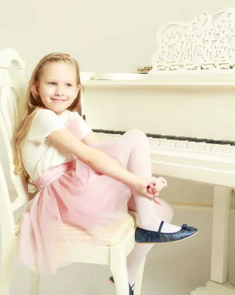 Uma menina está sentada no piano branco . — Fotografia de Stock